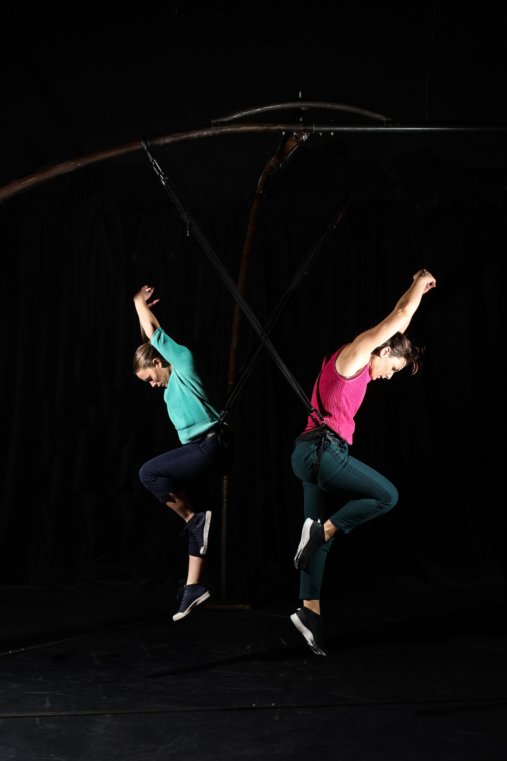 Deux personnes en tenue de sport sont suspendues dans les airs chacune levant les bras et les jambes dans une pose dynamique, créant un spectacle vivant saisissant.
