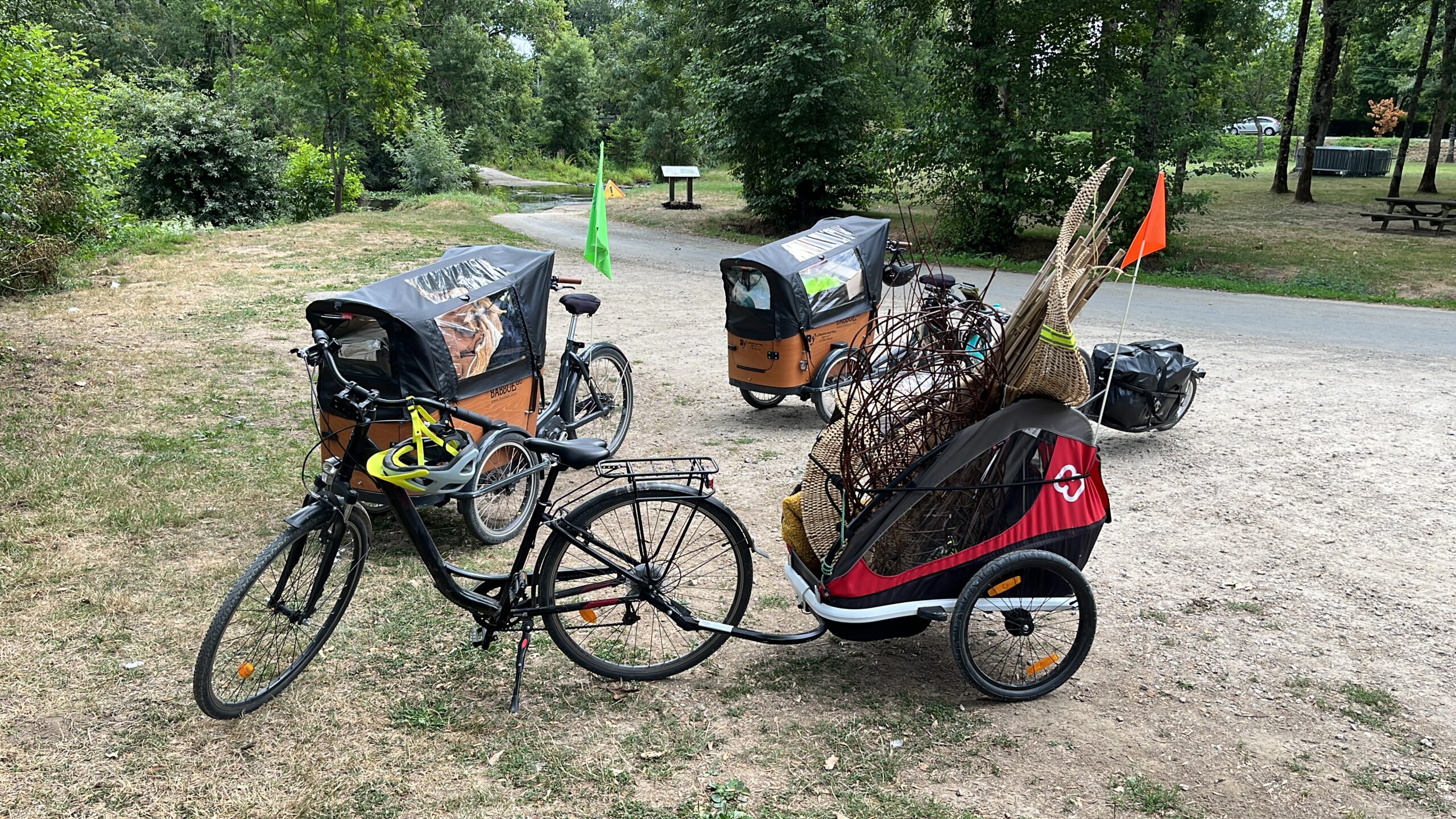 Trois vélos-cargos avec des remorques couvertes sont garés sur un chemin de terre dans une zone boisée, l'un d'eux transportant un chargement pour un spectacle éco-responsable
