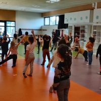 Un groupe d'enfants en maternelle participe à une activité de danse animée dans une salle de classe spacieuse et lumineuse, remplie d'équipements et d'étagères.